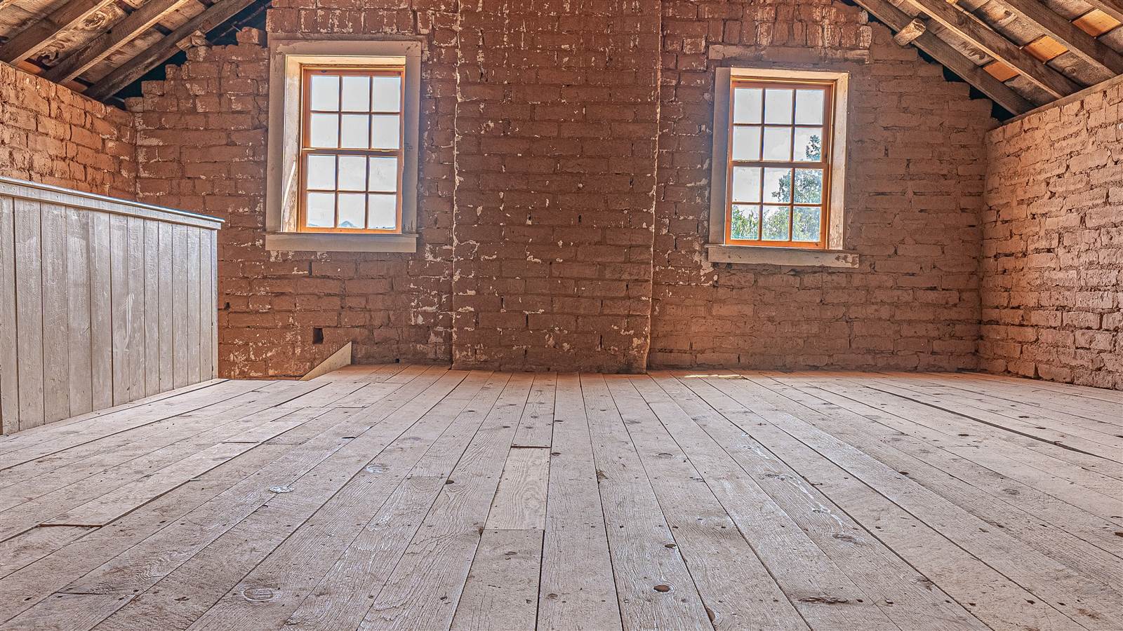 An empty attic with exposed roof rafters, brick walls and two windows
